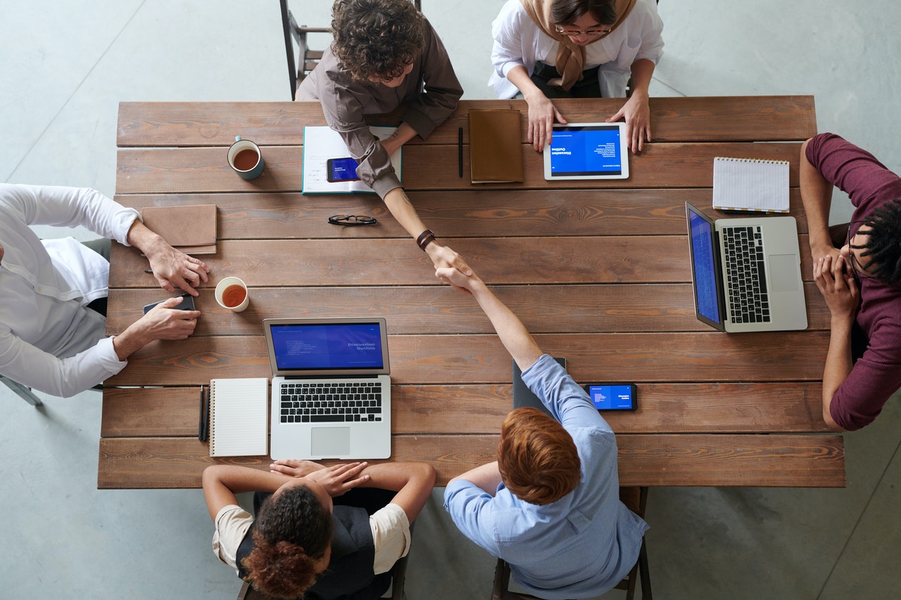 a group of people sitting around a table with laptops and a person standing on the floor with