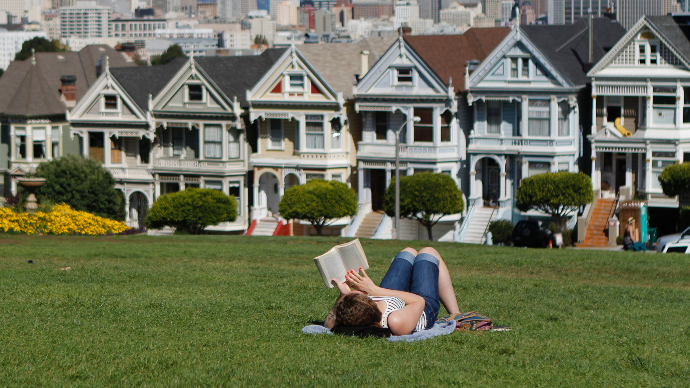 a person reading a book on the lawn in front of a house