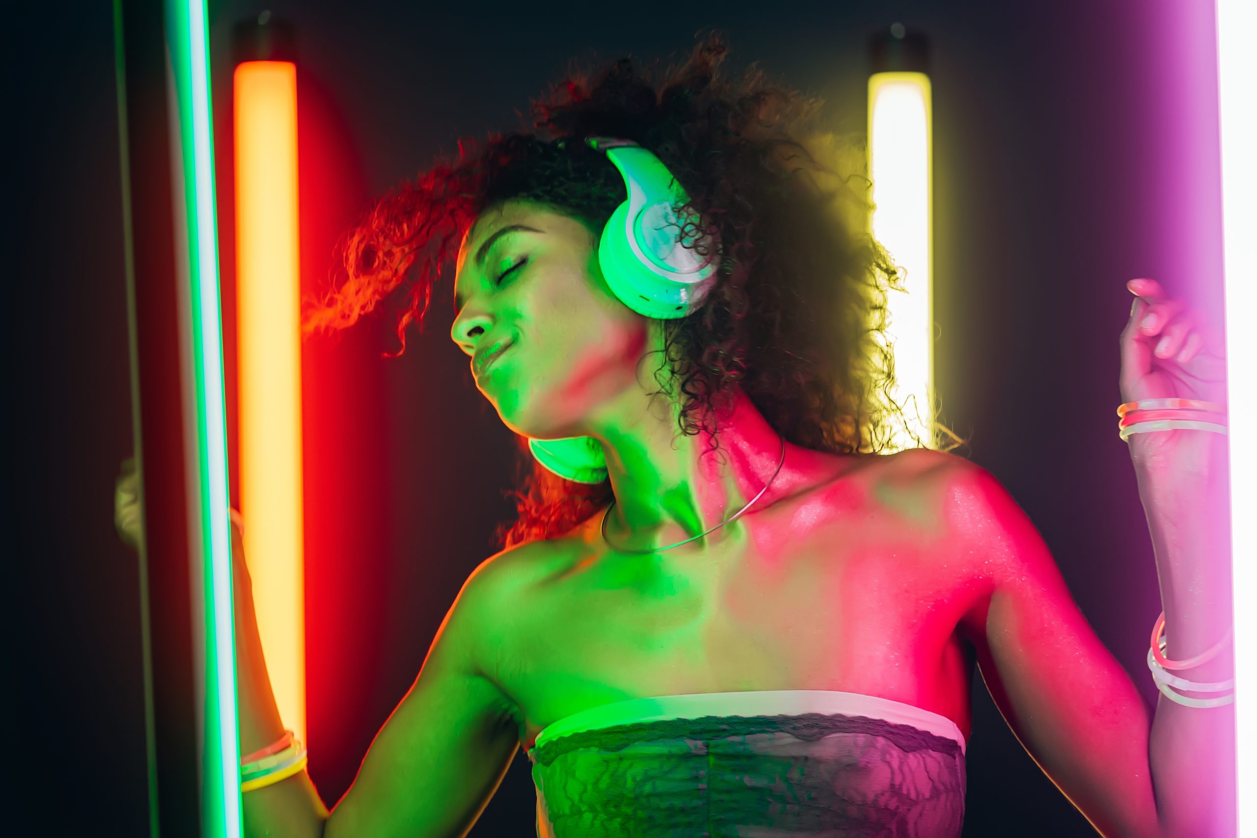 Portrait of party girl dancing to music with headphones on glowing multi-colored lamps in studio